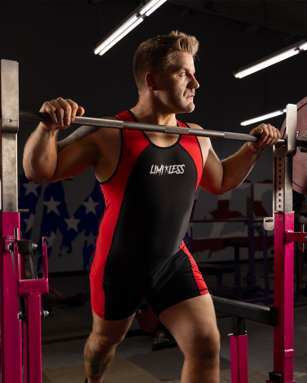 Man lifting weights in a gym wearing a red and black singlet with 'Limitless' branding.