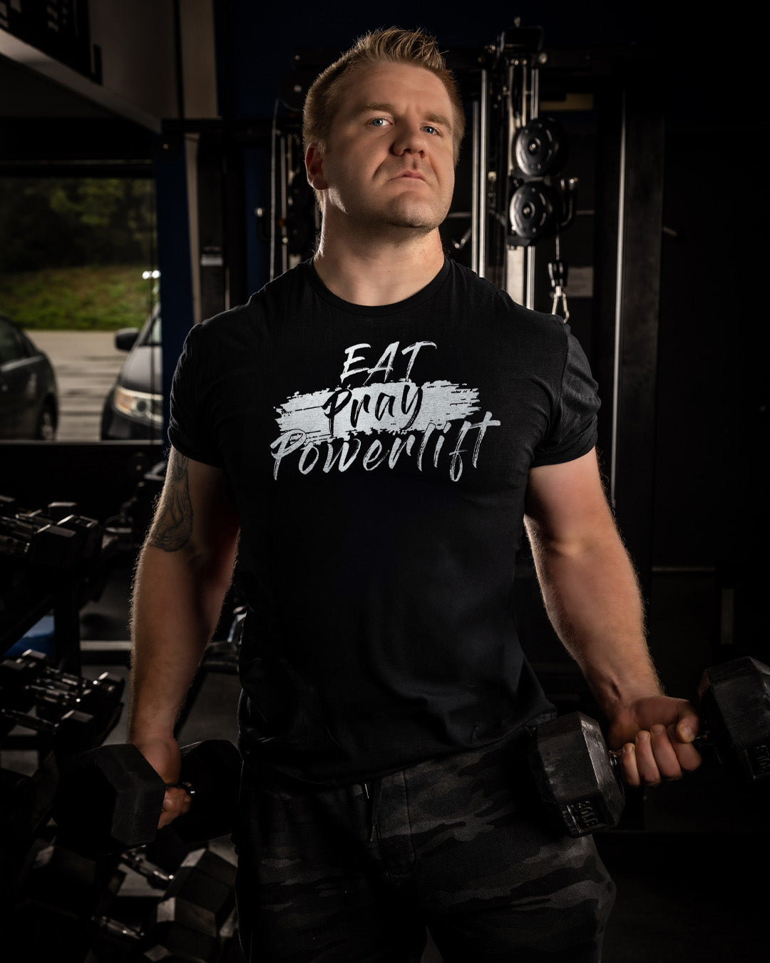 Man wearing a black t-shirt with 'EAT PRAY POWERLIFT' text in a gym setting