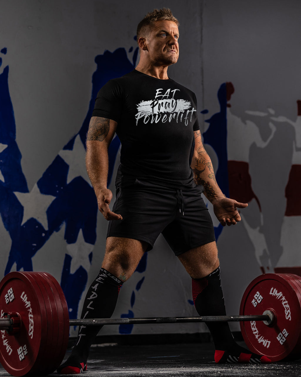 Man lifting weights with a motivational shirt in front of abstract wall art