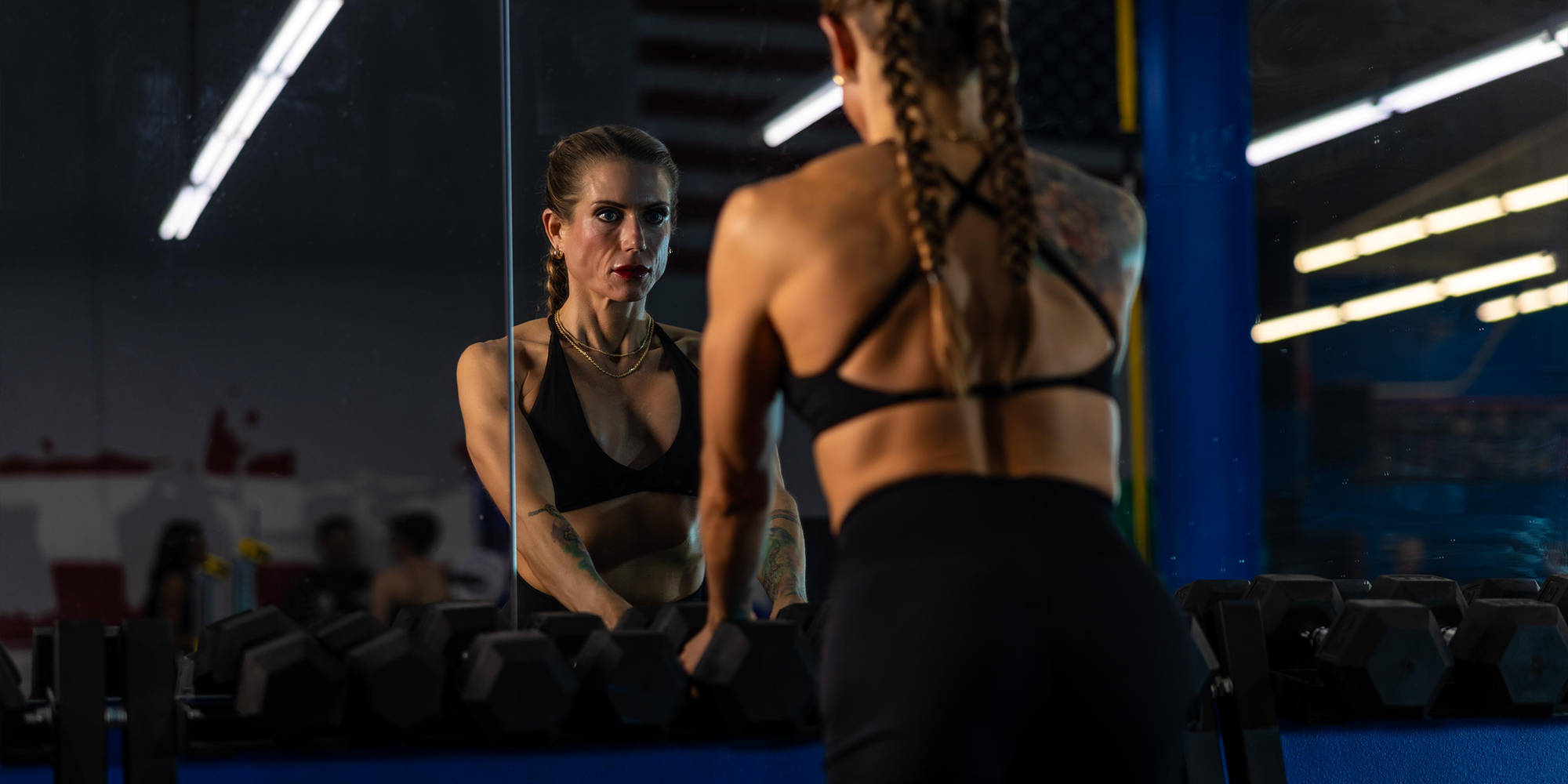 Woman in athletic wear looking at herself in a mirror in a gym setting