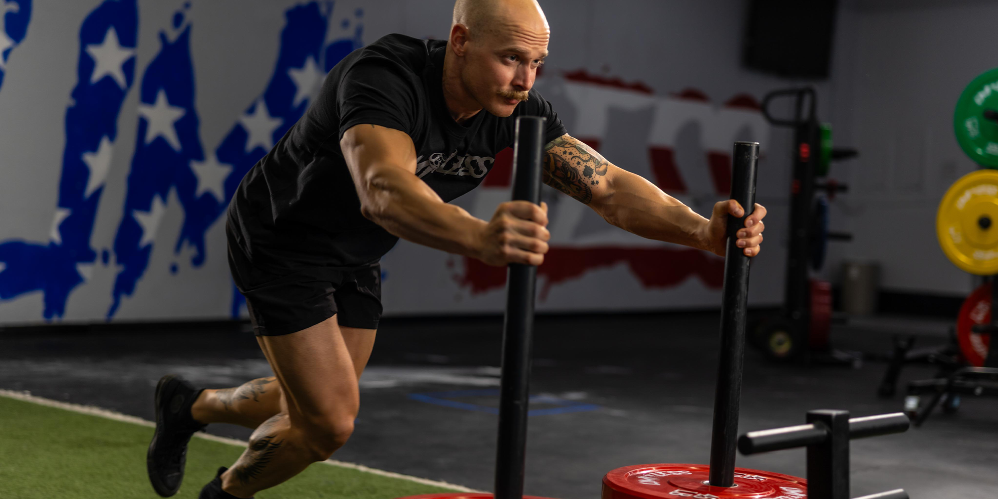 Man exercising with weights in a gym setting with a Limitless american flag mural