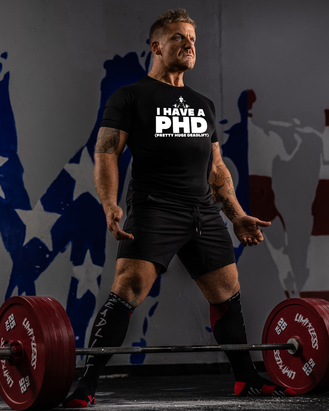 Man lifting weights with a humorous 'I have a PhD' t-shirt in a gym setting