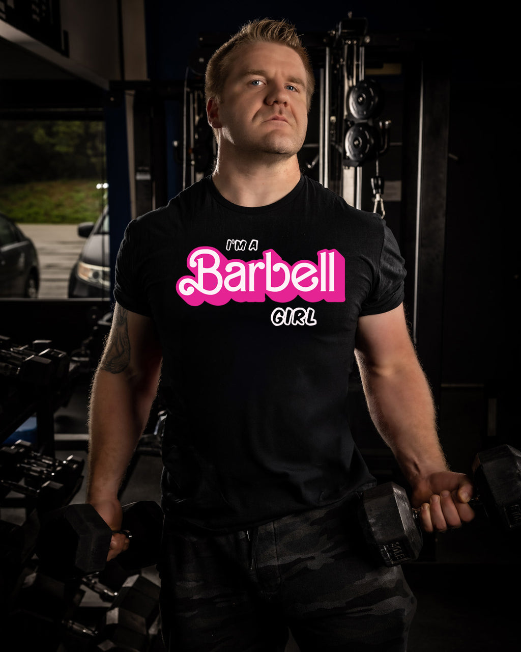 Person wearing a black t-shirt with 'I'm a Barbell Girl' text in pink and white, standing in a gym.