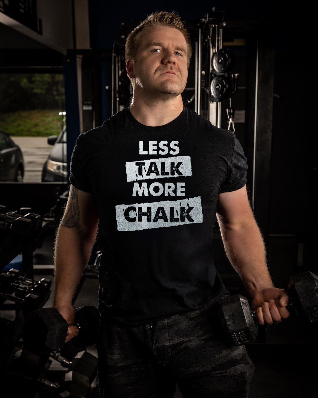 Man wearing a black t-shirt with 'LESS TALK MORE CHALK' text in a gym setting