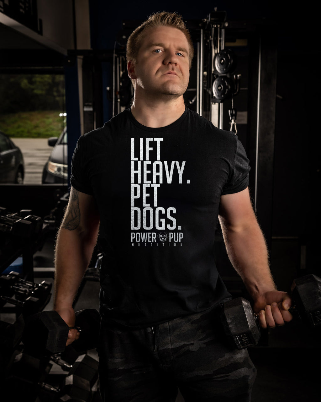 Man wearing a black t-shirt with 'LIFT HEAVY. PET DOGS.' text in a gym setting