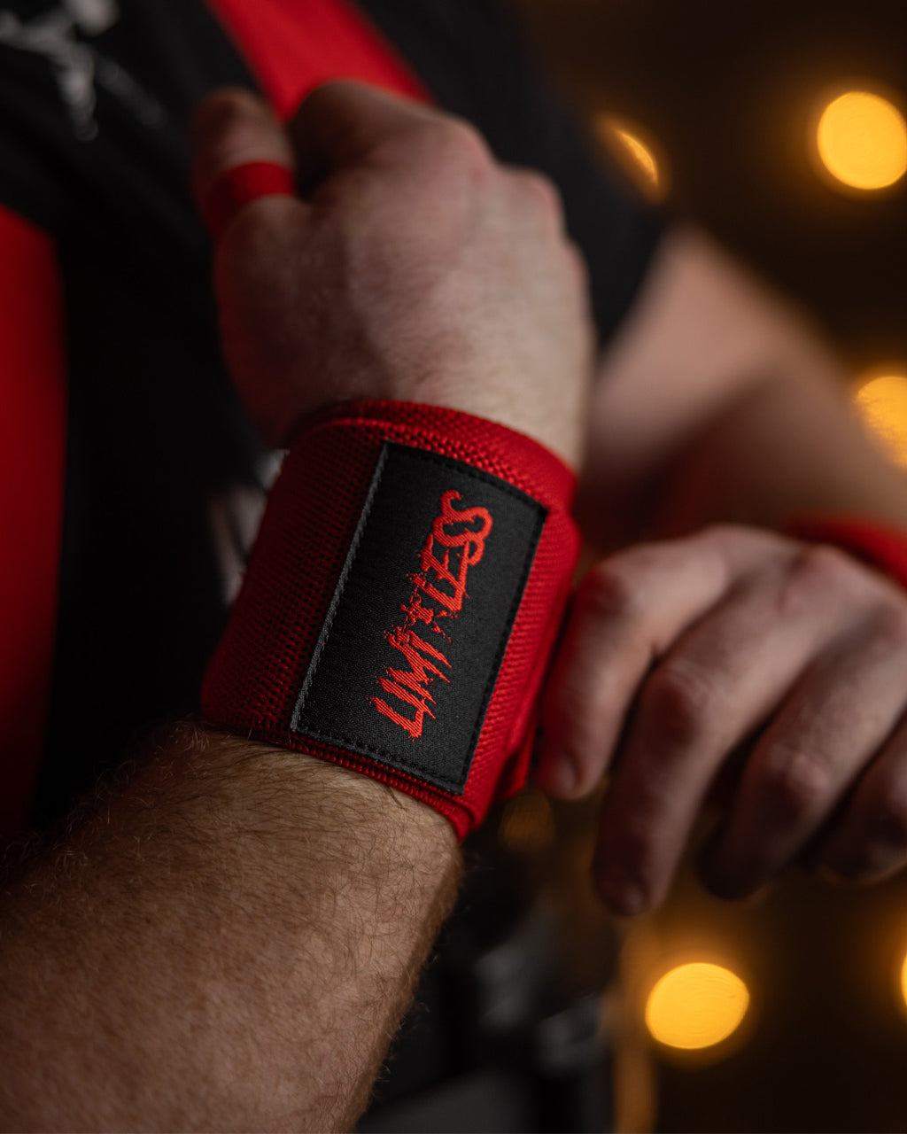 Red wrist wrap with black Limitless logo on a person's wrist against a blurred background