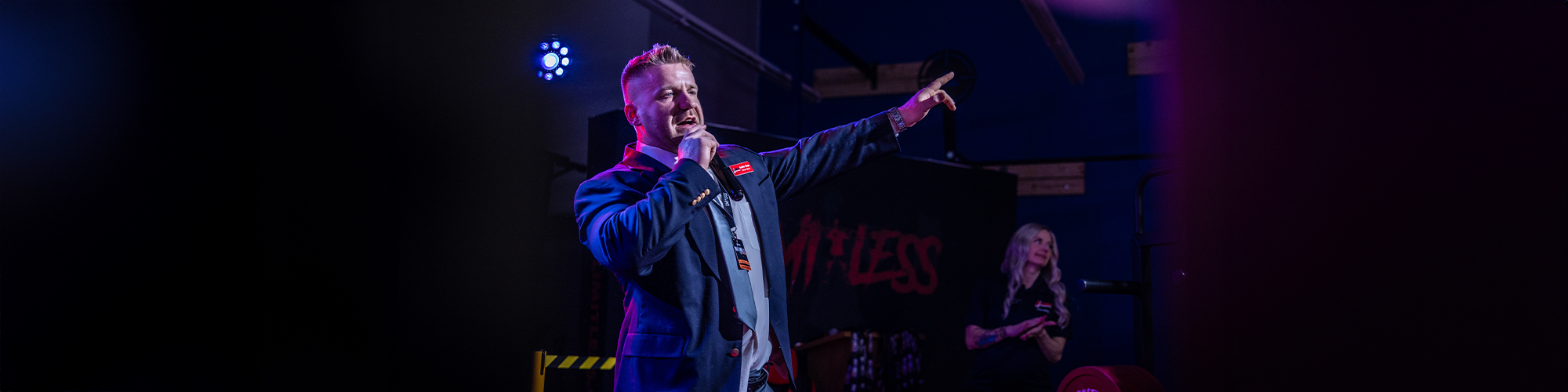 Man on stage with microphone pointing upwards, dark background