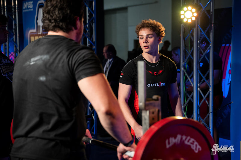 Person lifting a barbell with a spotter in a weightlifting competition setting