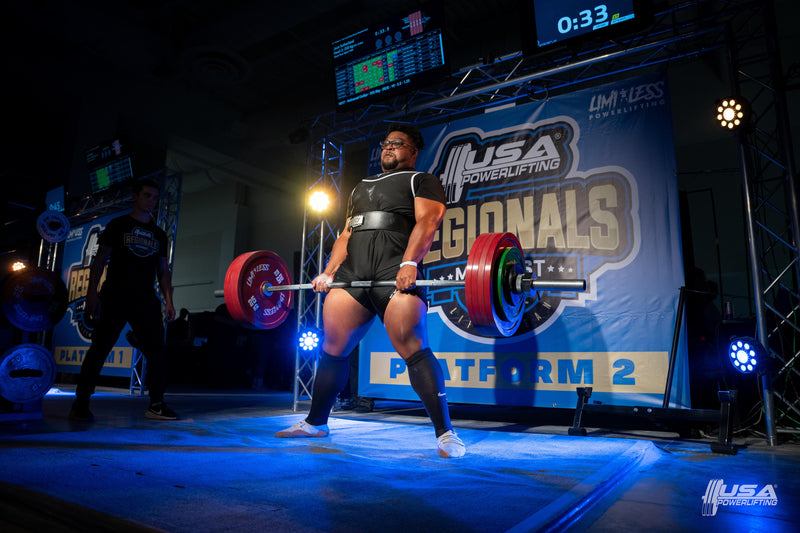 Person lifting a barbell at a powerlifting competition with 'USA Powerlifting' branding.
