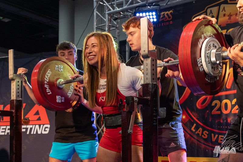 Athlete lifting a barbell with red weights at USA Powerlifting Olympia Open hosted by Limitless Powerlifting