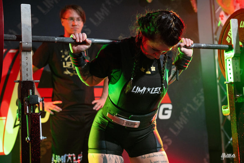 Person lifting a barbell with 'LIMITESS' branding in a gym setting