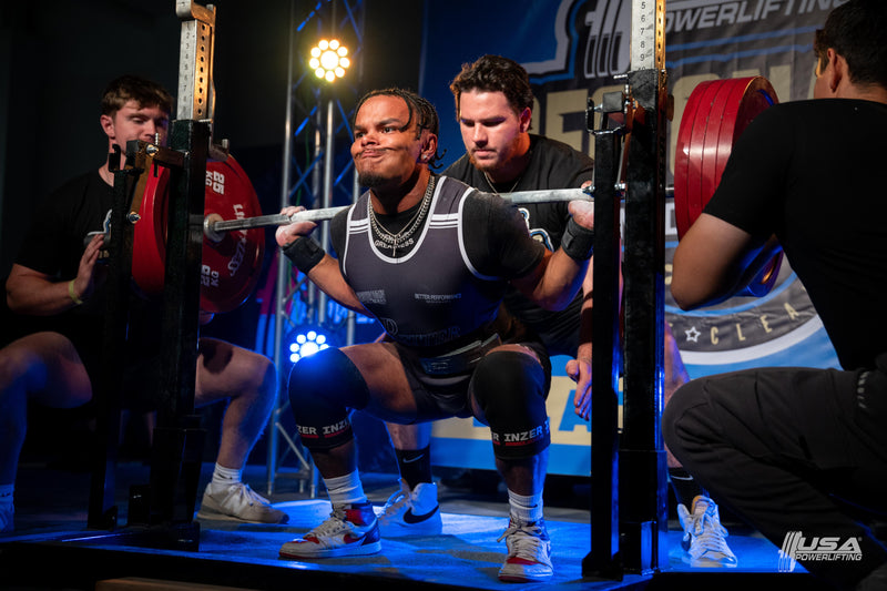 Powerlifter performing a squat lift with support from coaches in a weightlifting competition.  At USA Powerlifting Midwest Regionals hosted by Limitless Powerlifting