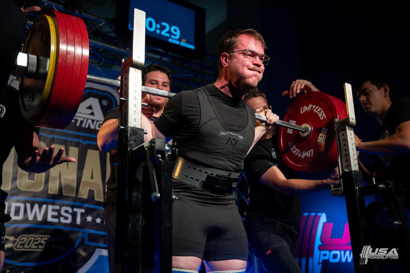 Athlete lifting weights with support personnel in a weightlifting competition setting.  USA powerlifting Midwest regionals Limitless Powerlifting