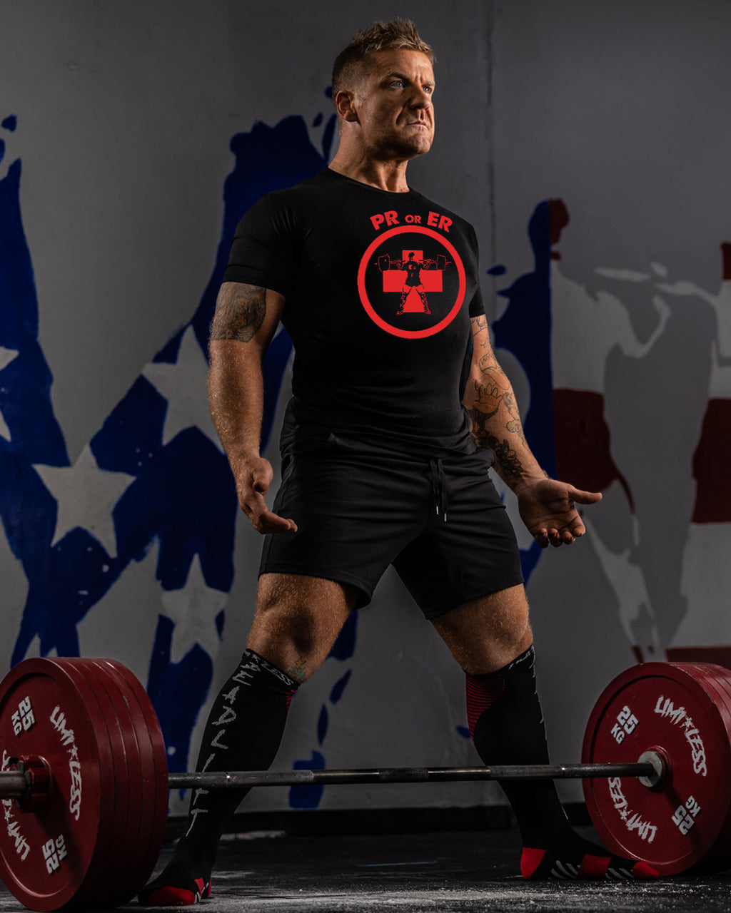 Man lifting weights with a black t-shirt featuring a red logo against a dark background