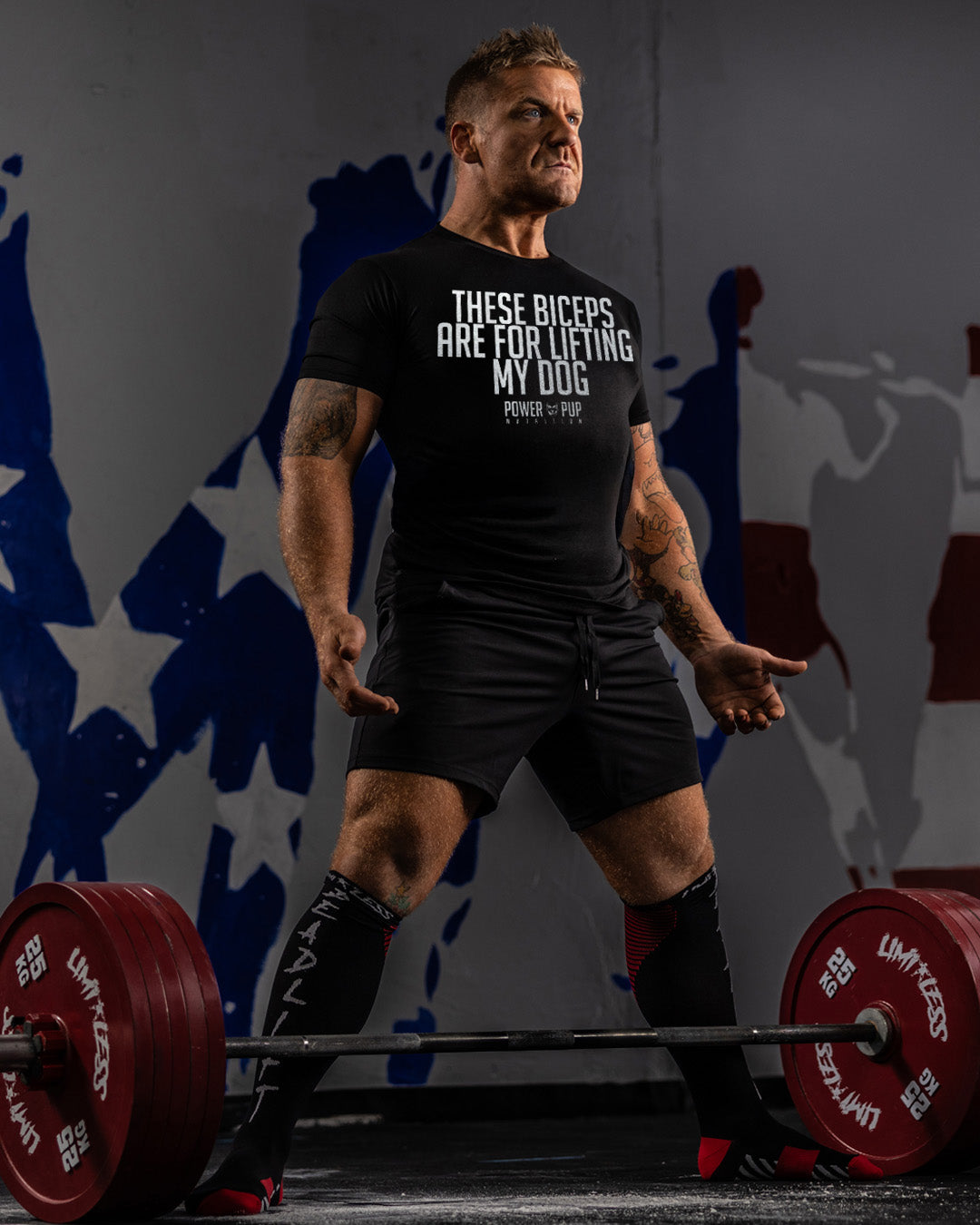 Man lifting weights with a humorous t-shirt in front of abstract wall art