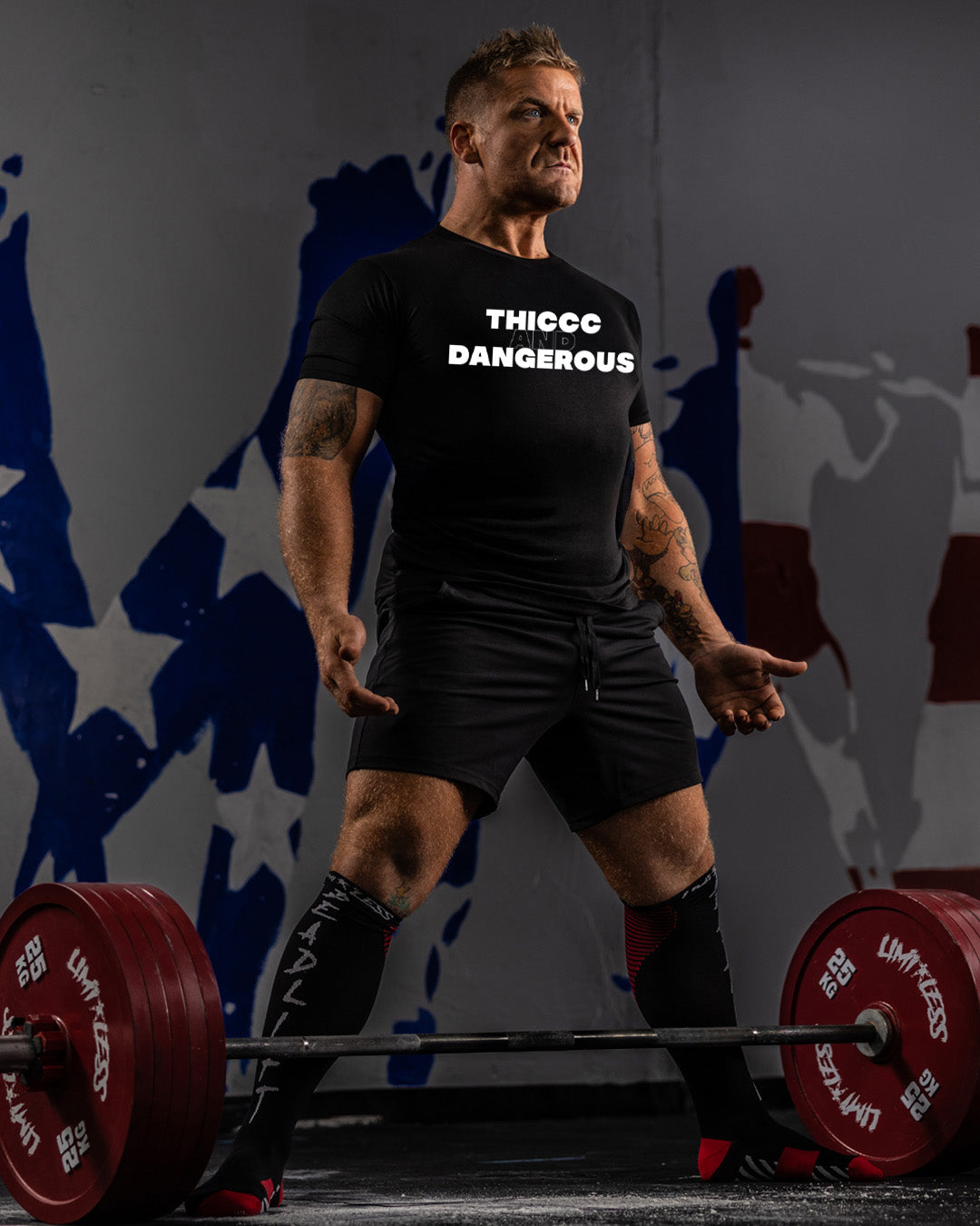 Man lifting weights with a black t-shirt displaying 'THICC DANGEROUS' text.