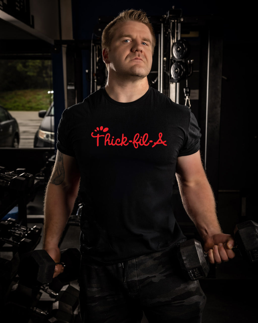 Man wearing a black t-shirt with red text in a garage setting thick-fil-a