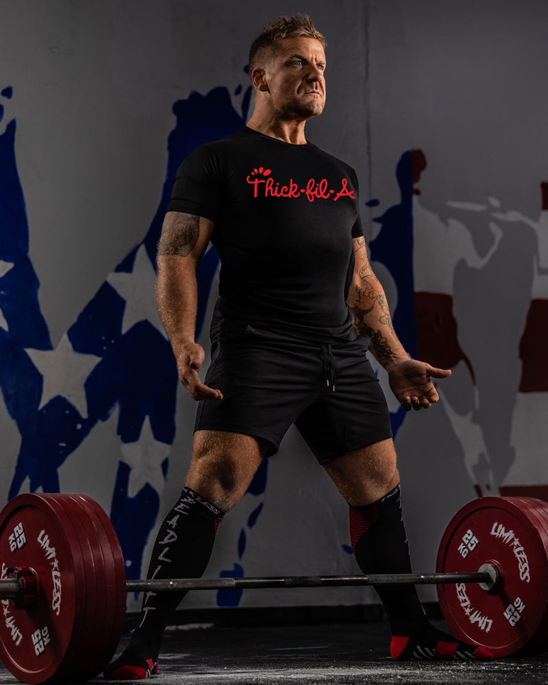Man lifting weights with a 'Thick-fil-a' t-shirt in front of a colorful abstract background
