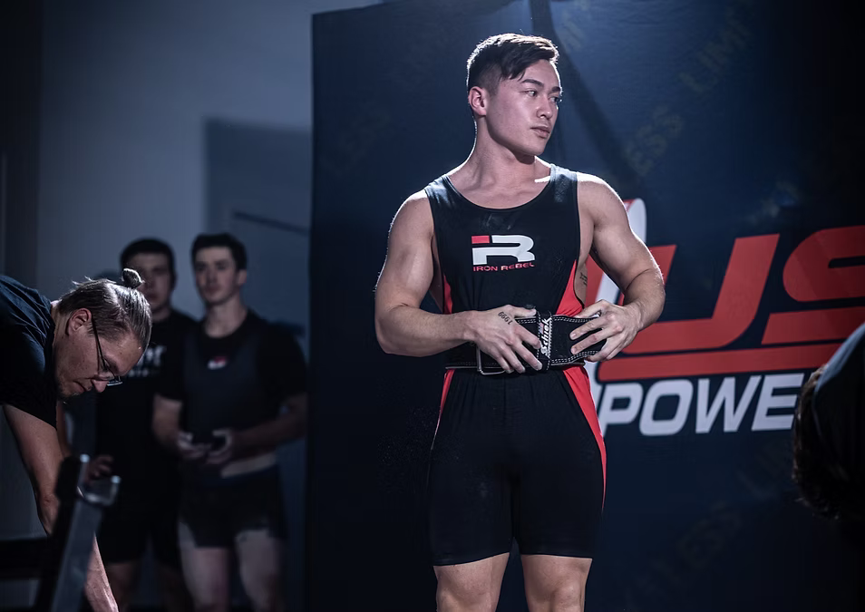 Person in a black and red athletic outfit with a visible brand logo, standing in front of a branded backdrop.