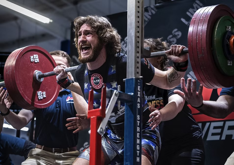 Athlete lifting a barbell with red weight plates in a gym setting at limitless powerlifting meet